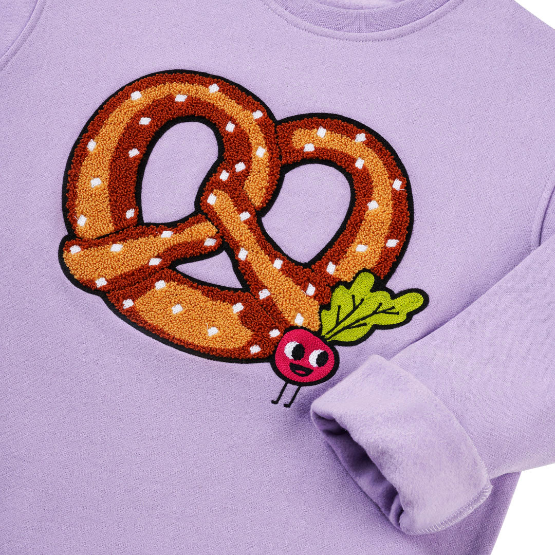 Detailansicht: Hochwertige Stickerei Brezel mit kleinen Radieschen auf lavendelfarbenem CHIO MI Kindersweatshirt – Close-up pretzel and radish embroidery detail – Détail de broderie bretzel et radis de haute qualité.