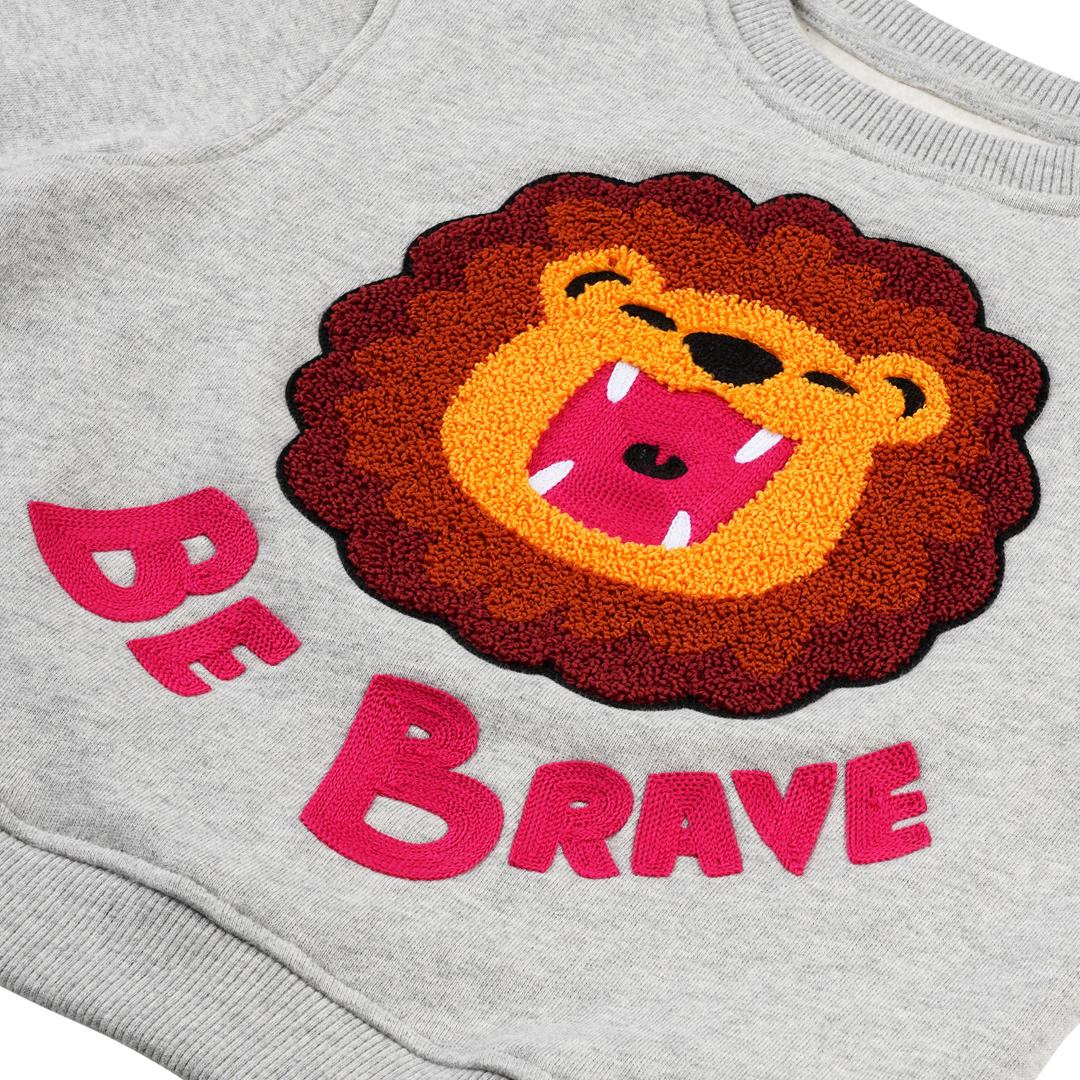 Detailansicht: Hochwertiger „Be Brave“ Schriftzug und detailreiche Löwen-Stickerei auf CHIO MI Sweater – Close-up "Be Brave" lion embroidery – Détail de broderie lion et texte "Be Brave" de haute qualité.
